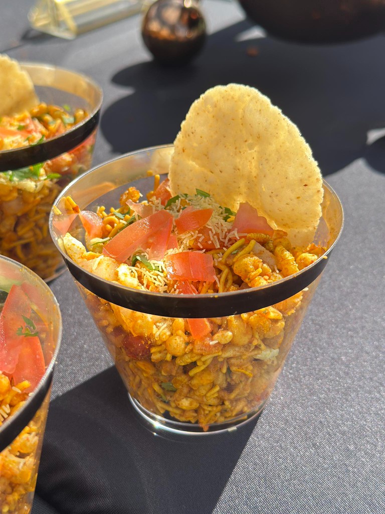 Bhel puri chaat served in a glass with crispy sev, fresh tomatoes, and papad